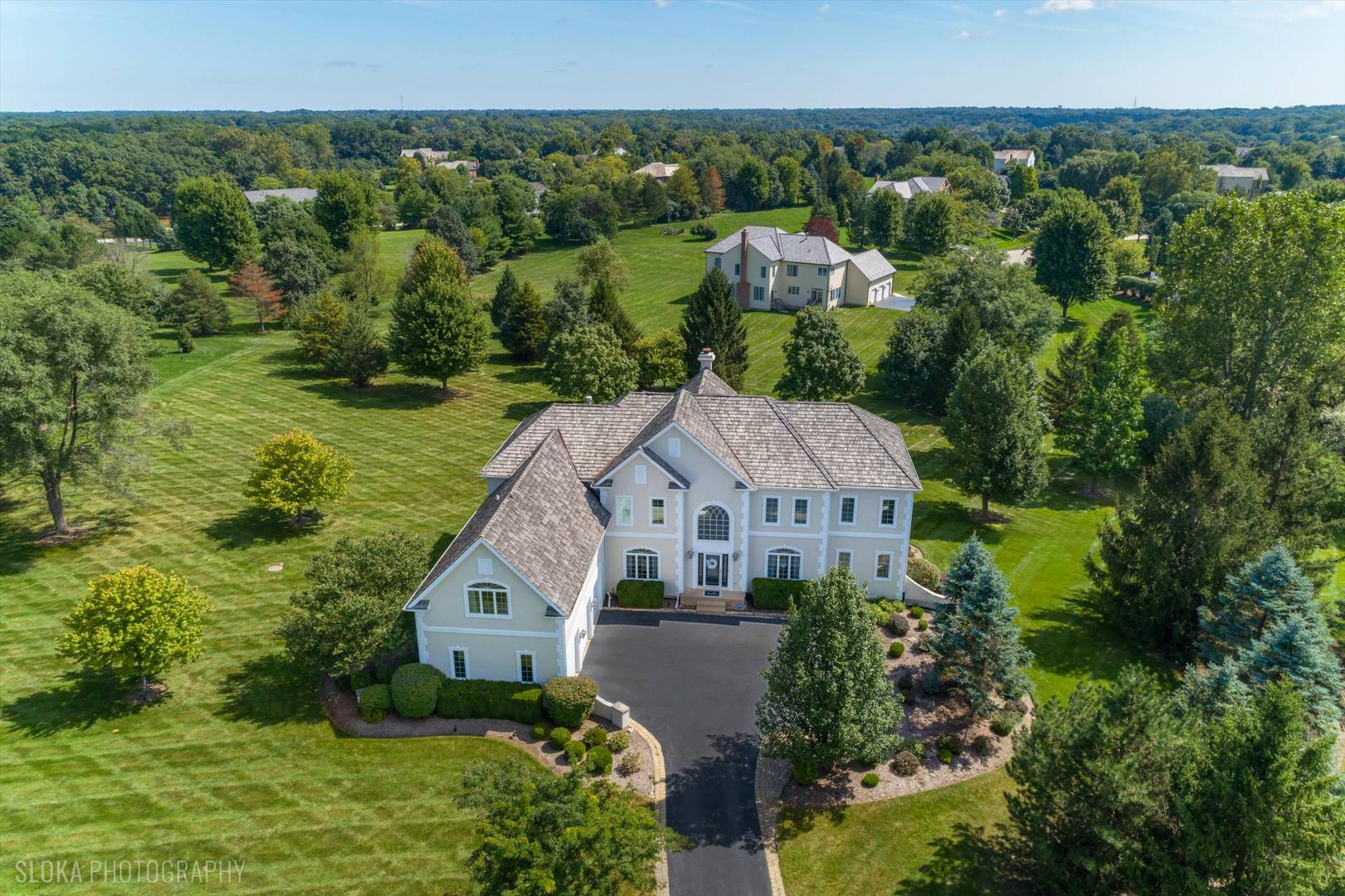 Aerial view of a large luxury home with expansive lawn, mature trees, and a circular driveway.