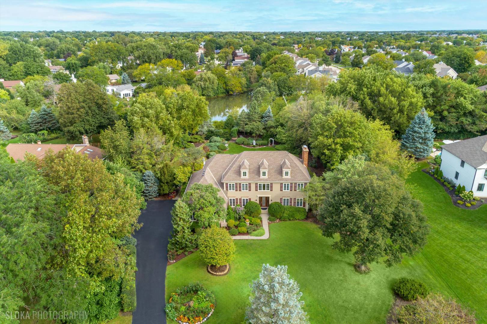 Aerial view of a large home with landscaped grounds, mature trees, and a pond nearby.