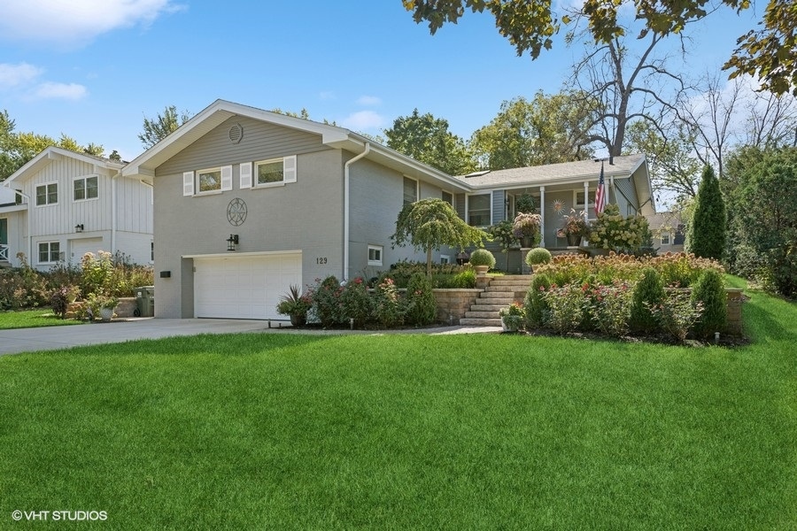 Gray split-level home with attached garage, landscaped flower beds, and a broad front lawn.