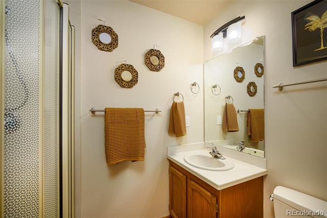 Bathroom with a wood vanity, large mirror, and glass-enclosed shower with a patterned panel.