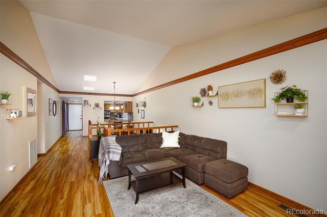 Living room with a brown sectional, area rug, and hardwood floors opening to the kitchen.