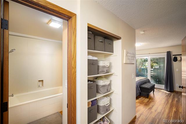 Built-in hallway shelving beside a bathroom doorway, with an adjoining room and hardwood floors.