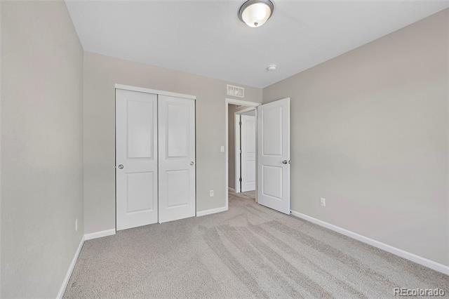Empty bedroom with beige carpet, a double closet, and an open hallway door.