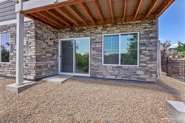 Covered stone patio with exposed timber ceiling, sliding glass door, and gravel ground.