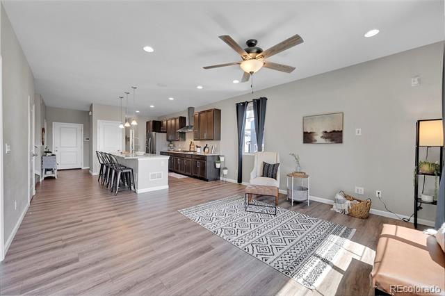 Open-plan living room and kitchen with a patterned rug, ceiling fan, and white island.