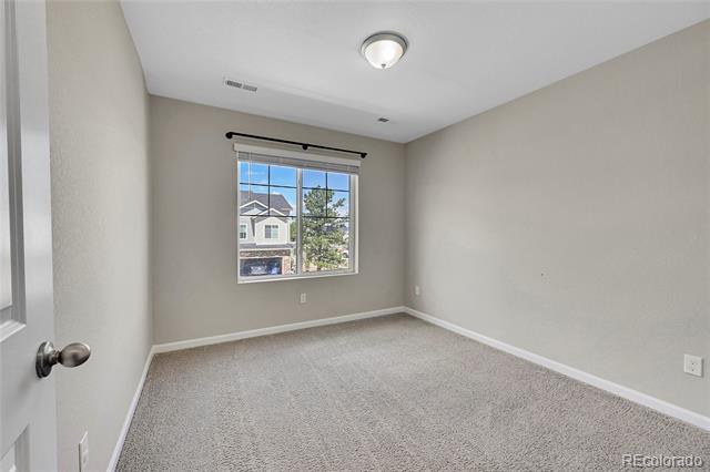 Vacant carpeted room with a large window overlooking neighboring homes and trees.