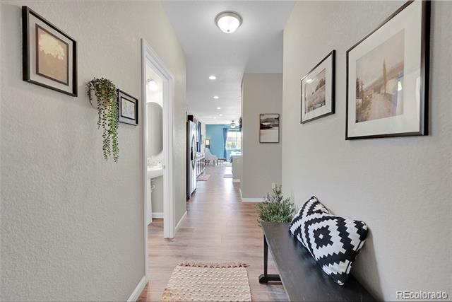 Hallway with light wood flooring, framed artwork, and a dark bench with patterned cushions.