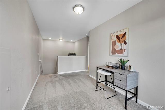 Carpeted entry hall with a half-height partition and a narrow desk beneath botanical artwork.