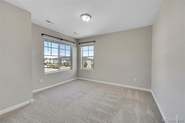 Empty carpeted bedroom with two windows overlooking neighboring homes.