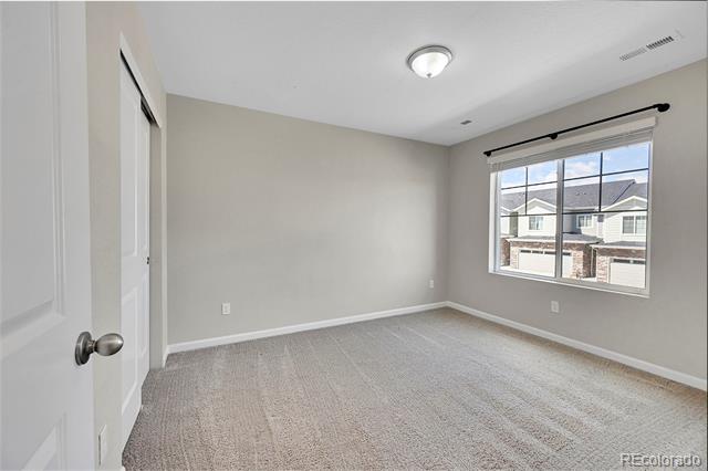 Empty carpeted bedroom with gray walls and a large window overlooking neighboring homes.