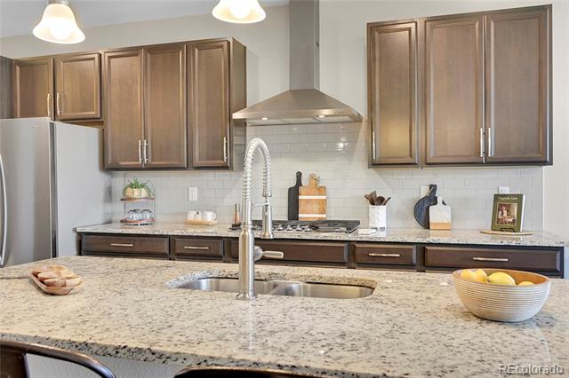 Kitchen with dark wood cabinets, granite island, double-basin sink, and stainless steel appliances.