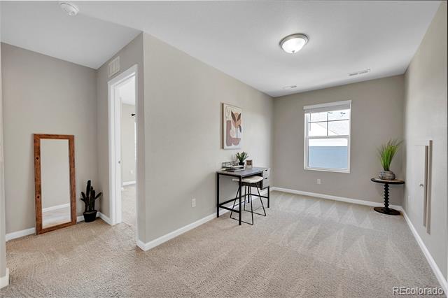Carpeted room with a small desk and stools, a window, and a leaning wood-framed mirror.