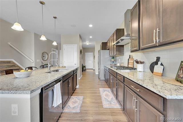 Galley kitchen with granite counters, dark wood cabinets, stainless appliances, and a long island.