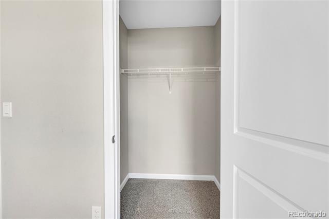 Empty walk-in closet with a white wire shelf and rod above gray carpet.