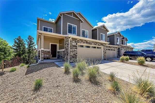 Two-story home with stone accents, attached garages, and a gravel front yard.