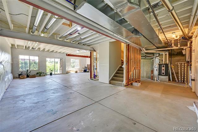 Unfinished basement with a broad concrete floor, exposed ductwork, and stairs beside mechanical equipment.