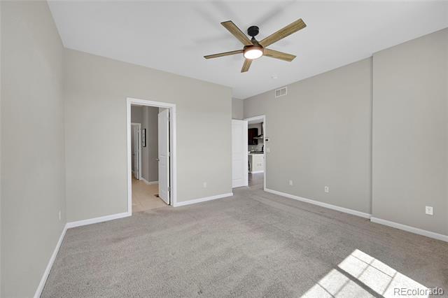Empty carpeted bedroom with a wood-blade ceiling fan and sunlight on the floor.