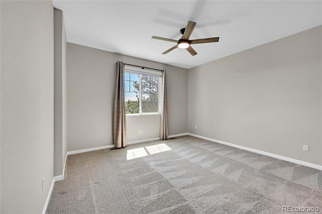 Empty bedroom with gray carpet, a curtained window, and a wood-blade ceiling fan.