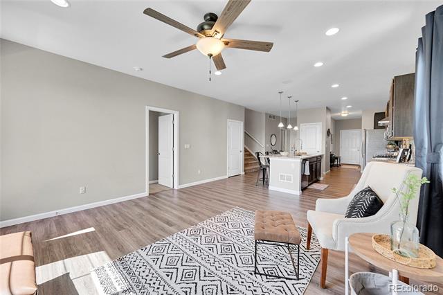 Open-plan living room and kitchen with geometric rug, white chairs, and a kitchen island.