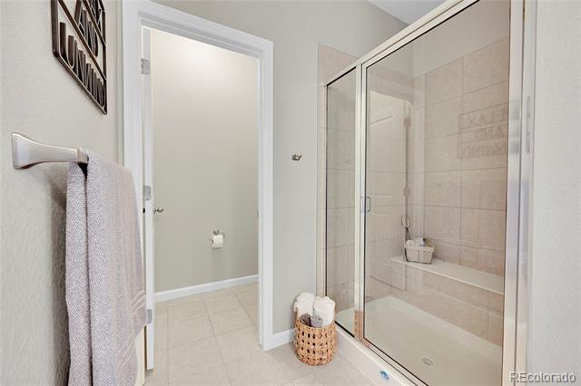 Bathroom with a glass-enclosed tiled shower and a basket of rolled towels.