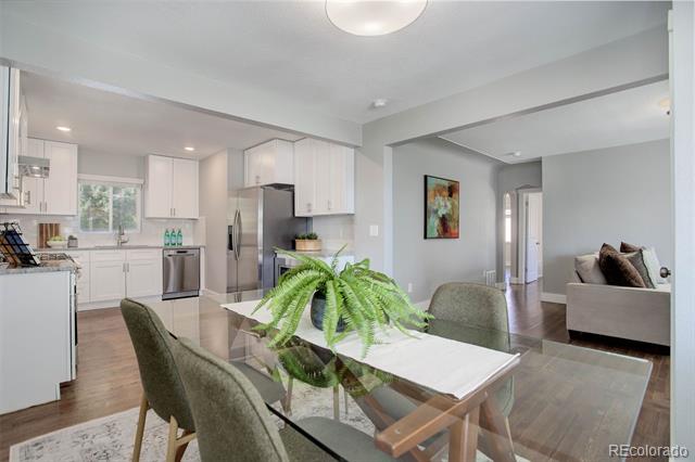 Open-plan dining area with a glass table and fern, beside a white kitchen and living room.