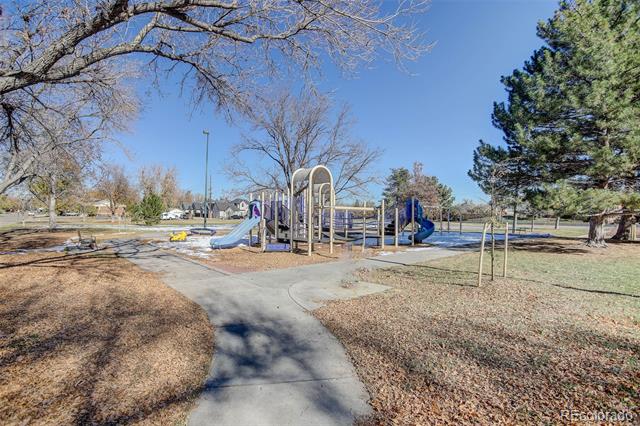 Neighborhood park with a colorful playground, paved paths, leafless trees, and open grassy areas.