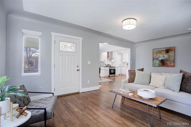 Staged living room with hardwood floors, a white sofa, and an open view into the kitchen.