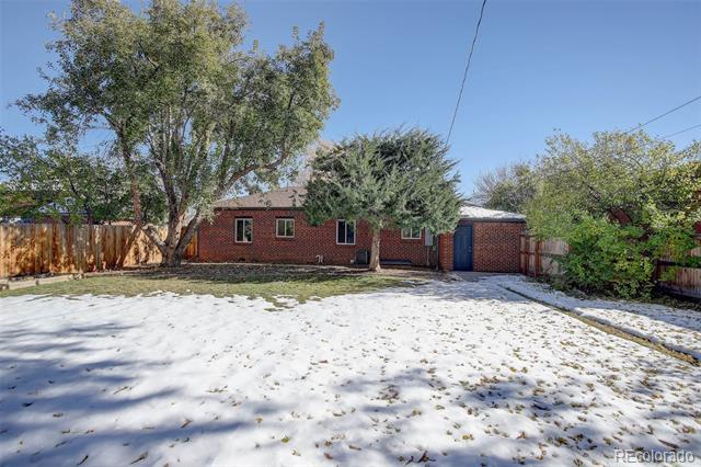 Rear of a brick home beyond a snow-covered yard, shaded by mature trees.