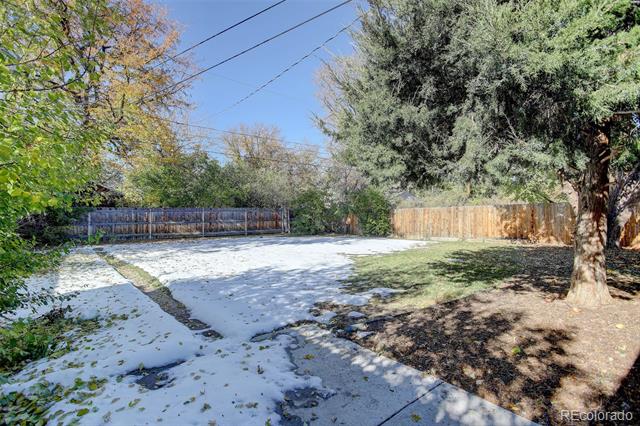 Snow-covered backyard with a paved patio, mature trees, and wooden fencing.