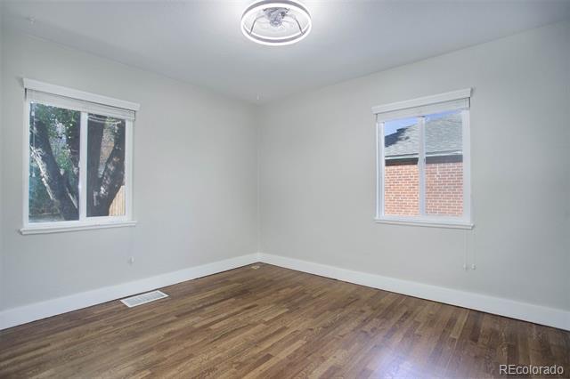 Empty bedroom with wood flooring and two windows.