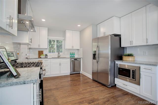 Bright white kitchen with stainless steel appliances, gray counters, and warm wood flooring.