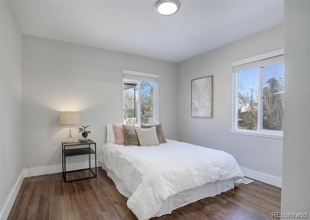 Bedroom with a white bed, two windows, and dark wood flooring.