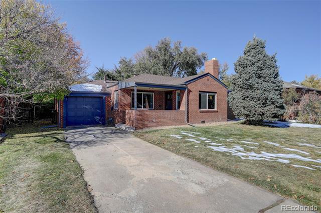 Red brick house with blue garage door and driveway, surrounded by mature trees and patches of snow.