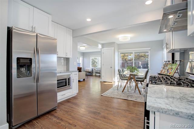 Open kitchen with stainless steel appliances, stone countertops, and a dining table by the windows.