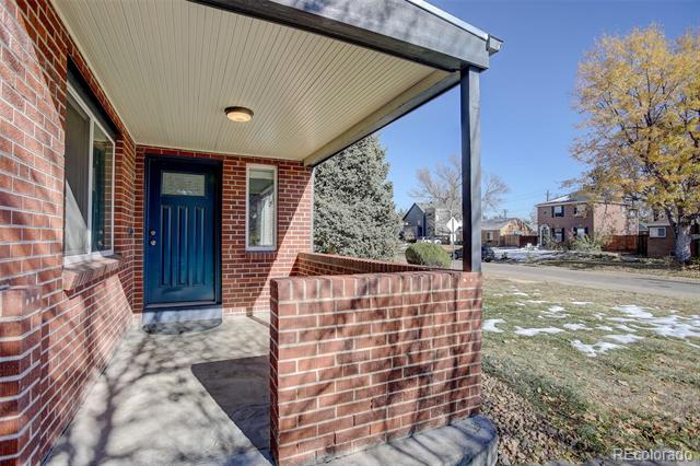 Red-brick home with a covered porch, blue front door, and patchy snow in the yard.