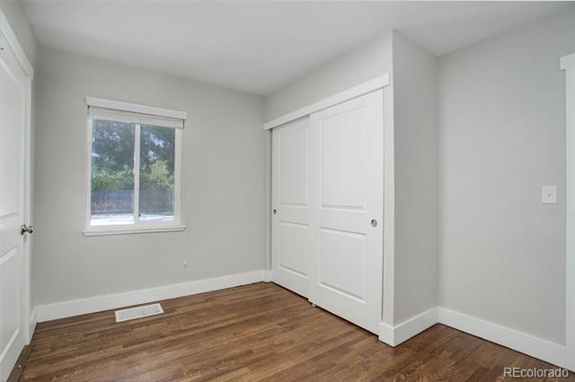 Empty bedroom with hardwood floors, a window, and white sliding closet doors.
