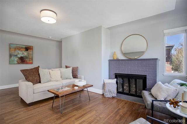 Living room with hardwood floors, white sofa, and purple brick fireplace beneath a round mirror.