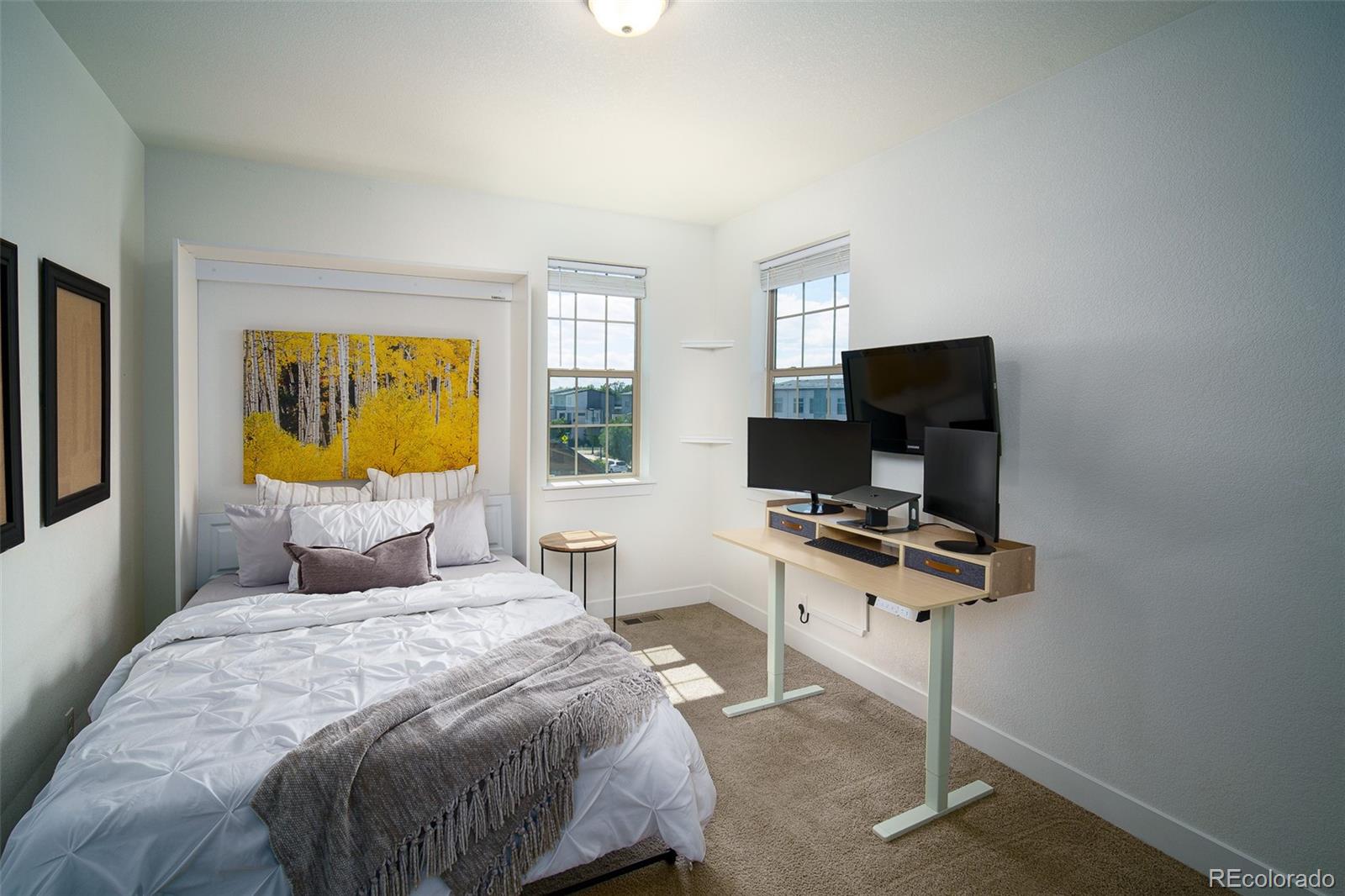 Bedroom with a white bed, yellow aspen artwork, and a standing desk with multiple monitors.