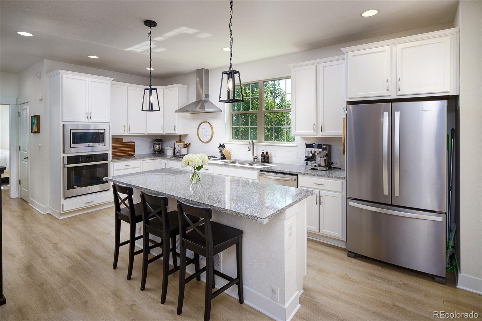 Bright kitchen with a granite island, white cabinets, stainless appliances, and black bar stools.