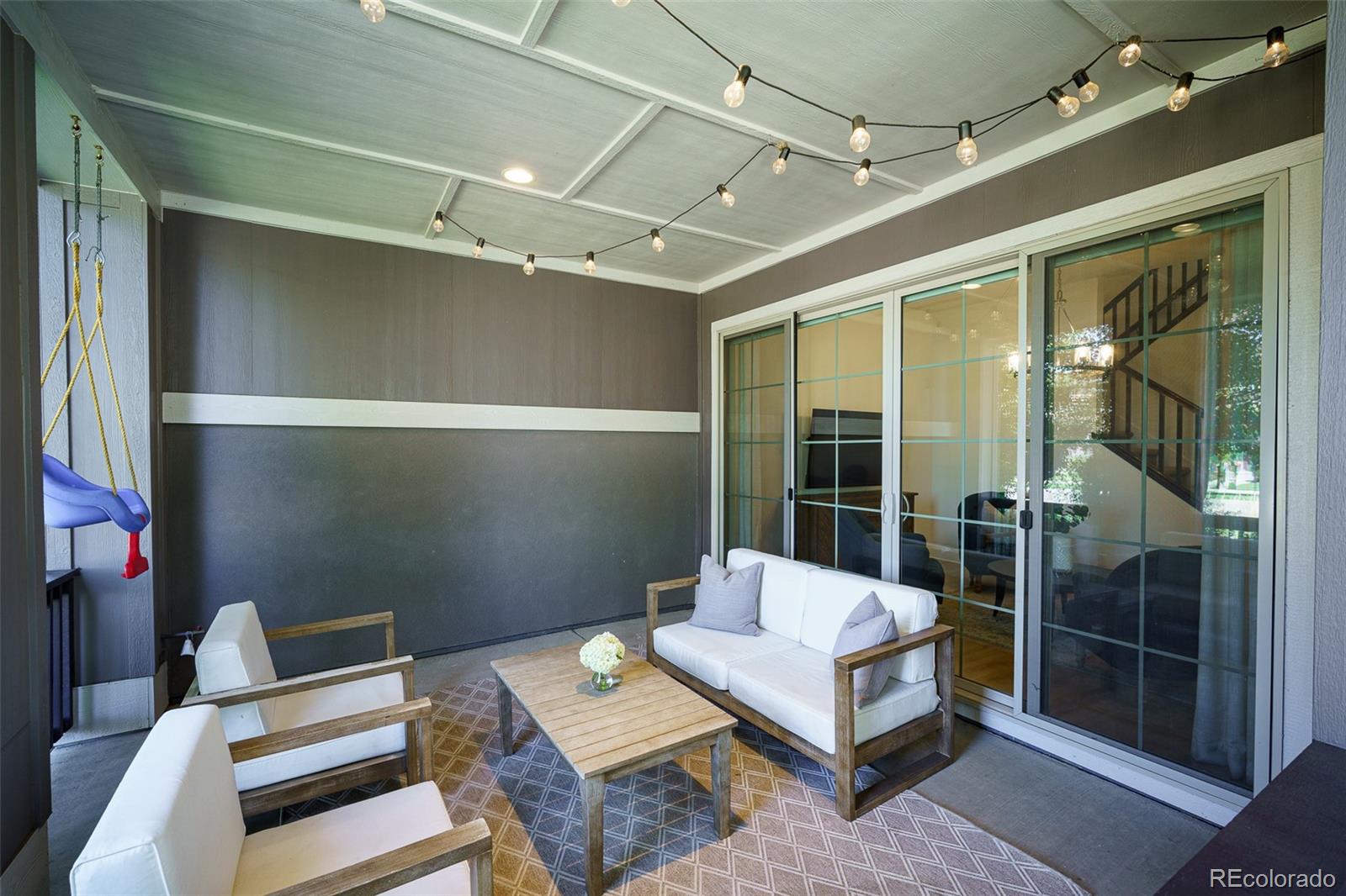Covered patio with cushioned seating, string lights, and sliding glass doors.