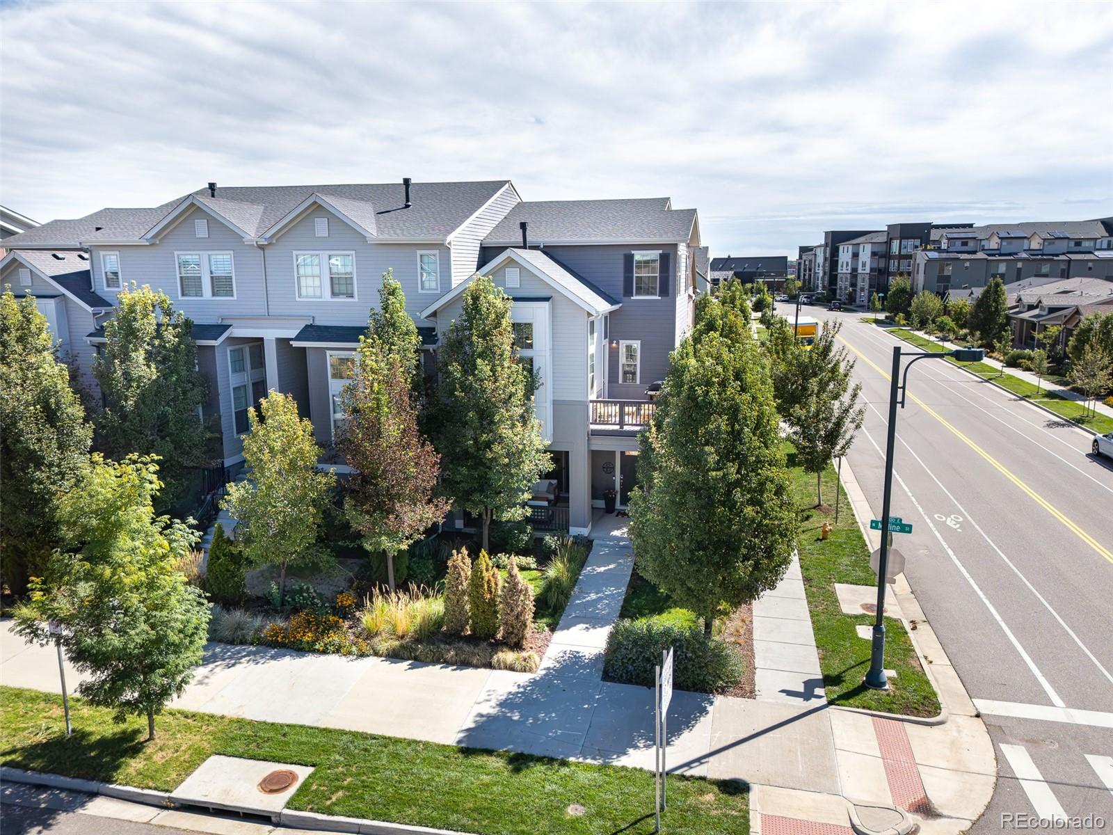 Gray multi-story townhouse on a landscaped corner lot beside a residential street.