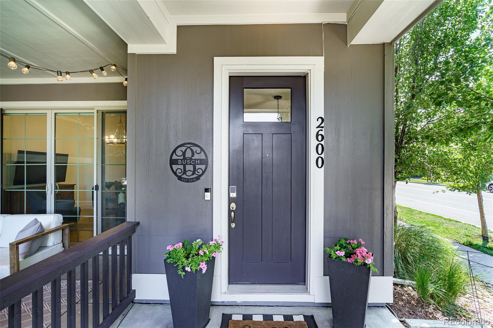 Home entrance with a dark purple door, white trim, and pink flowers in planters.