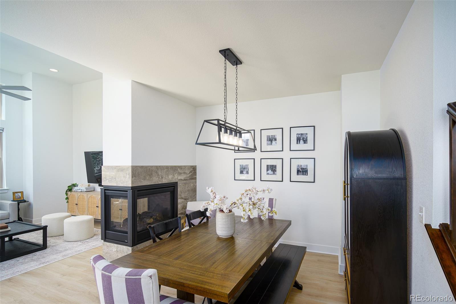 Dining area with a long wood table beside a stone-clad fireplace and open living room.