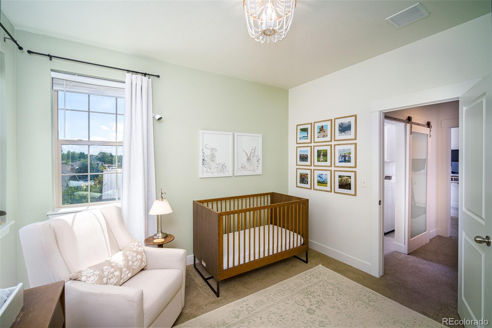 Nursery with a wooden crib, white armchair, and large curtained window.