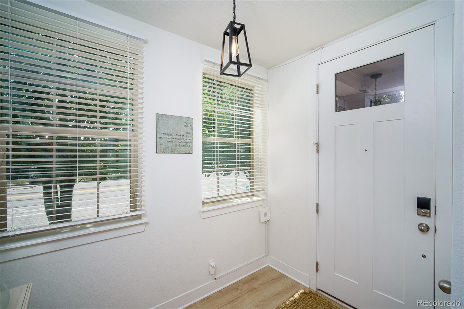 Bright entryway with a white paneled door, two blind-covered windows, and a black pendant light.
