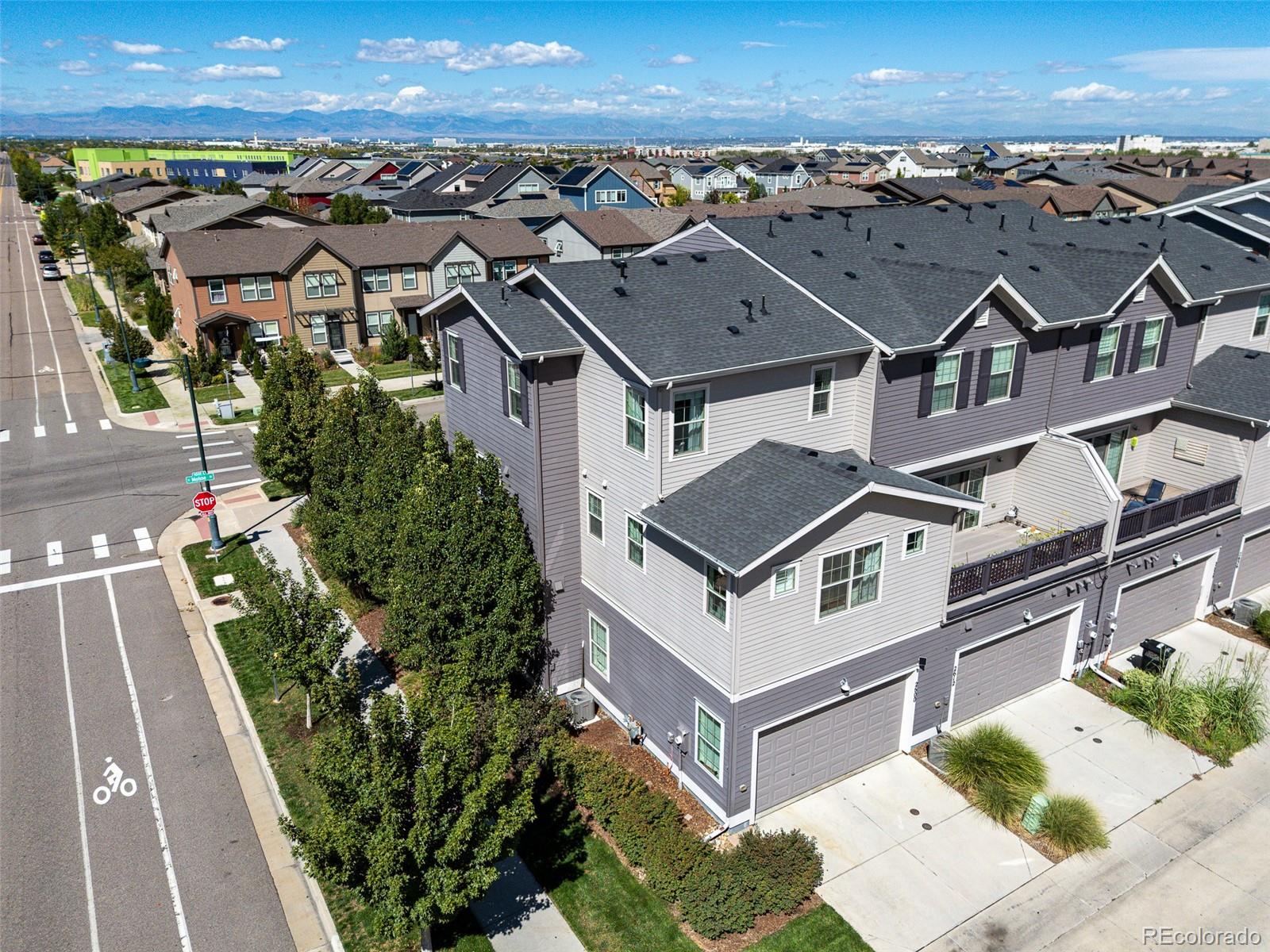 Gray multi-story townhome with attached garages, surrounded by homes and distant Rocky Mountains.