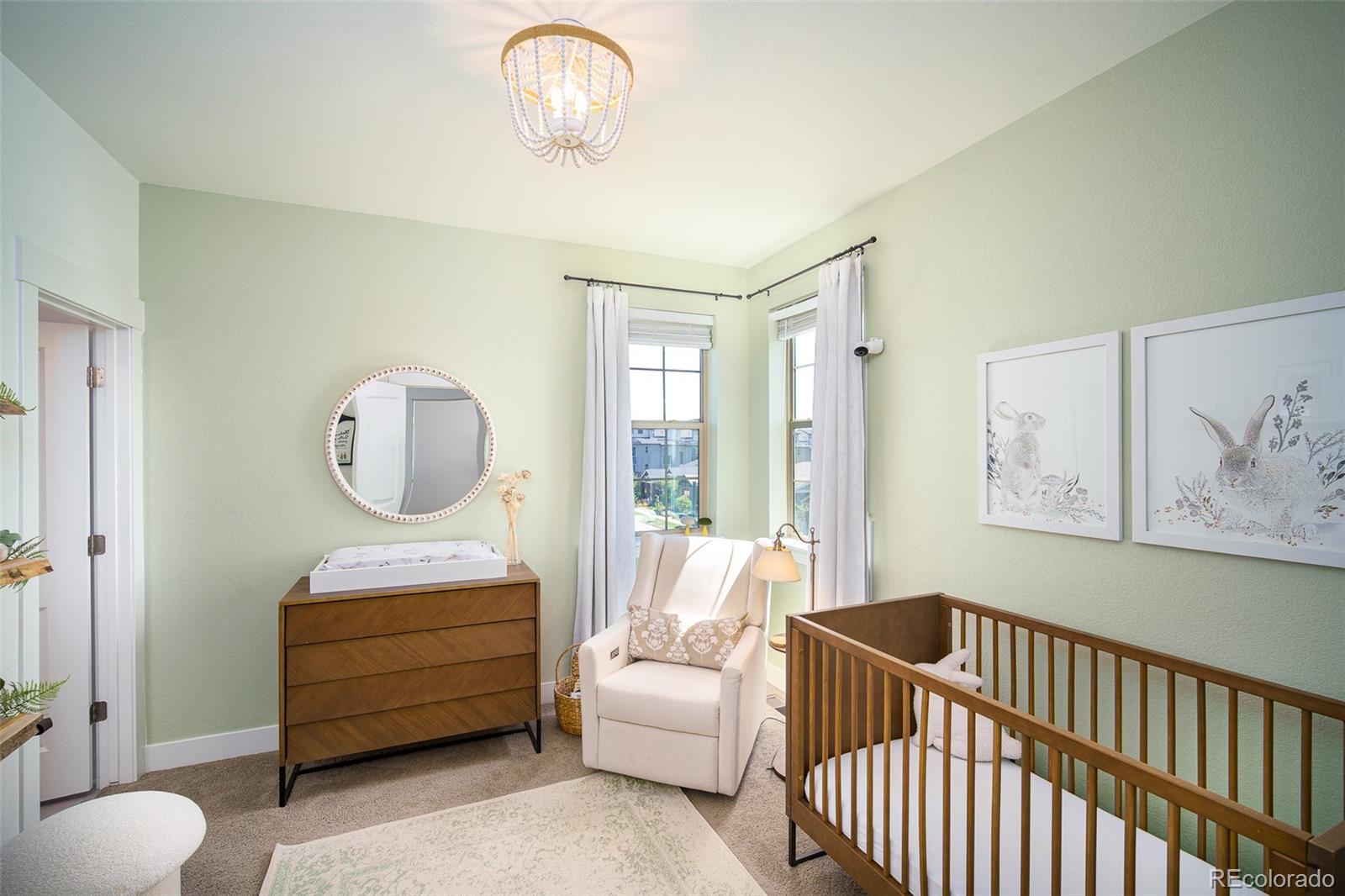 Nursery with a wooden crib, white rocking chair, and two tall curtained windows.