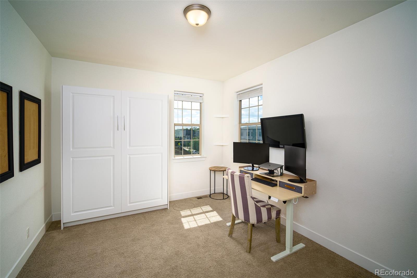 Home office with a Murphy bed cabinet, multi-monitor desk, and striped chair.