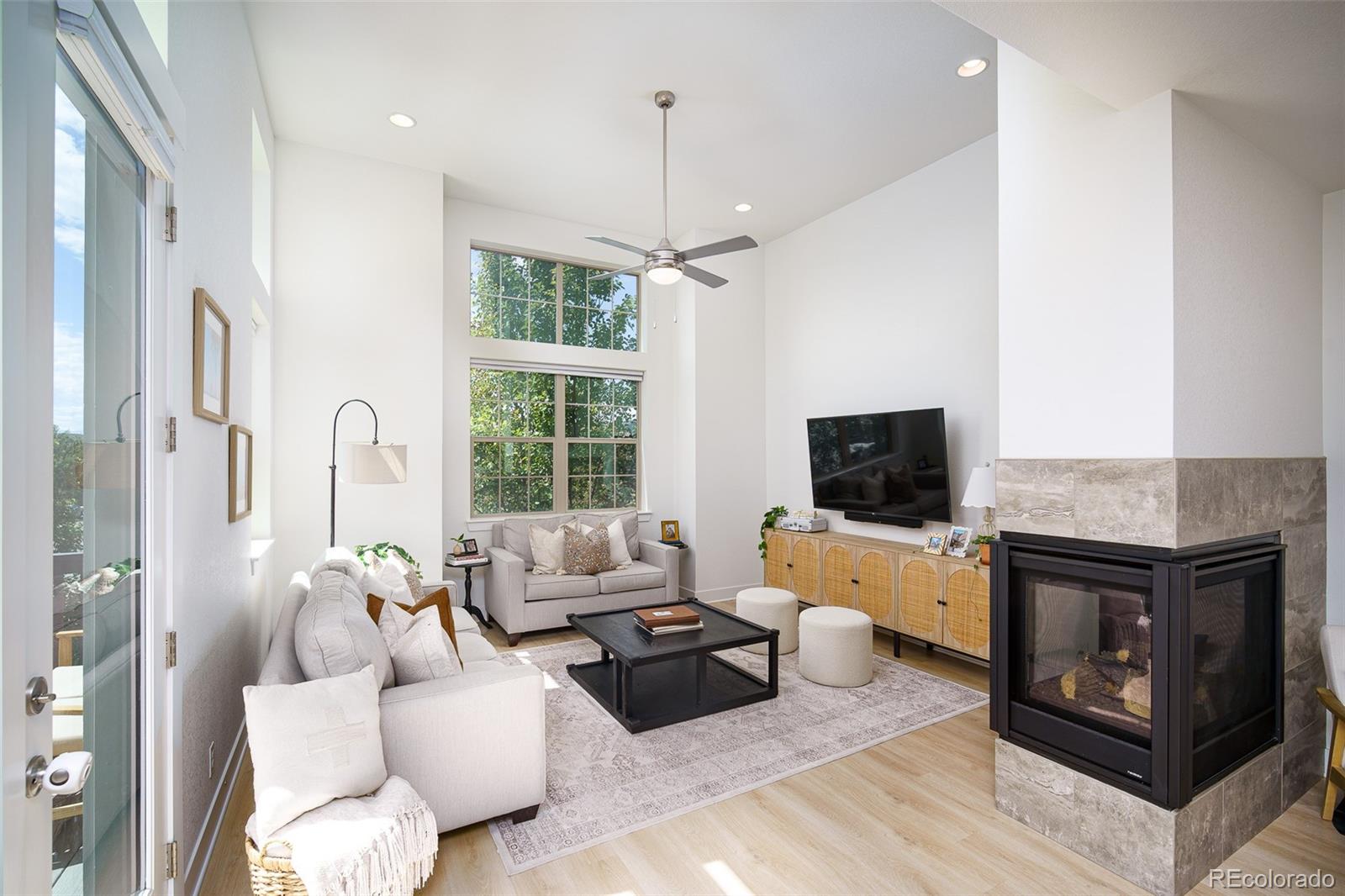 Living room with tall windows, light sofas, and a stone-surround fireplace.
