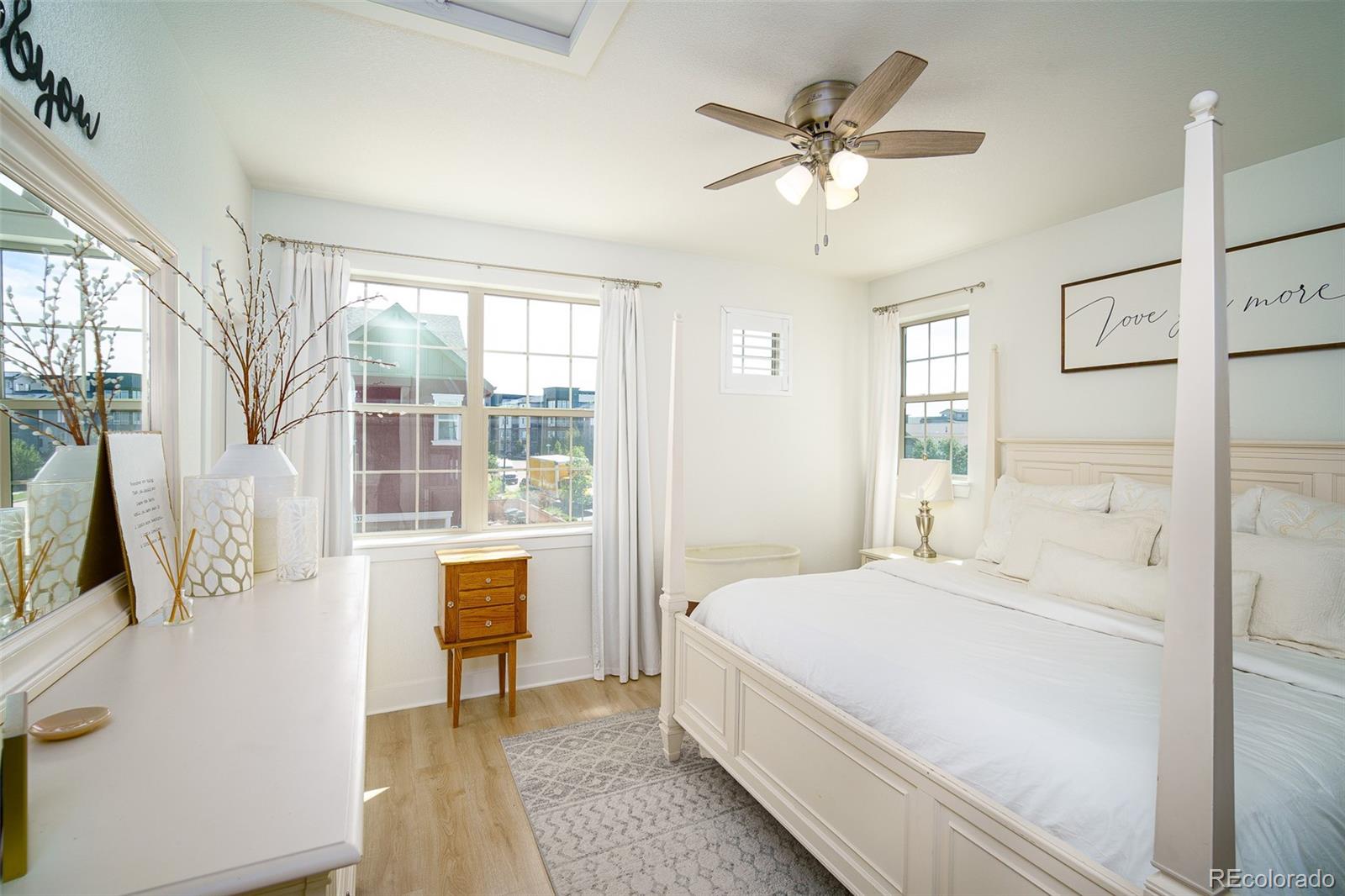 Bright bedroom with a white four-poster bed, large curtained windows, and ceiling fan.